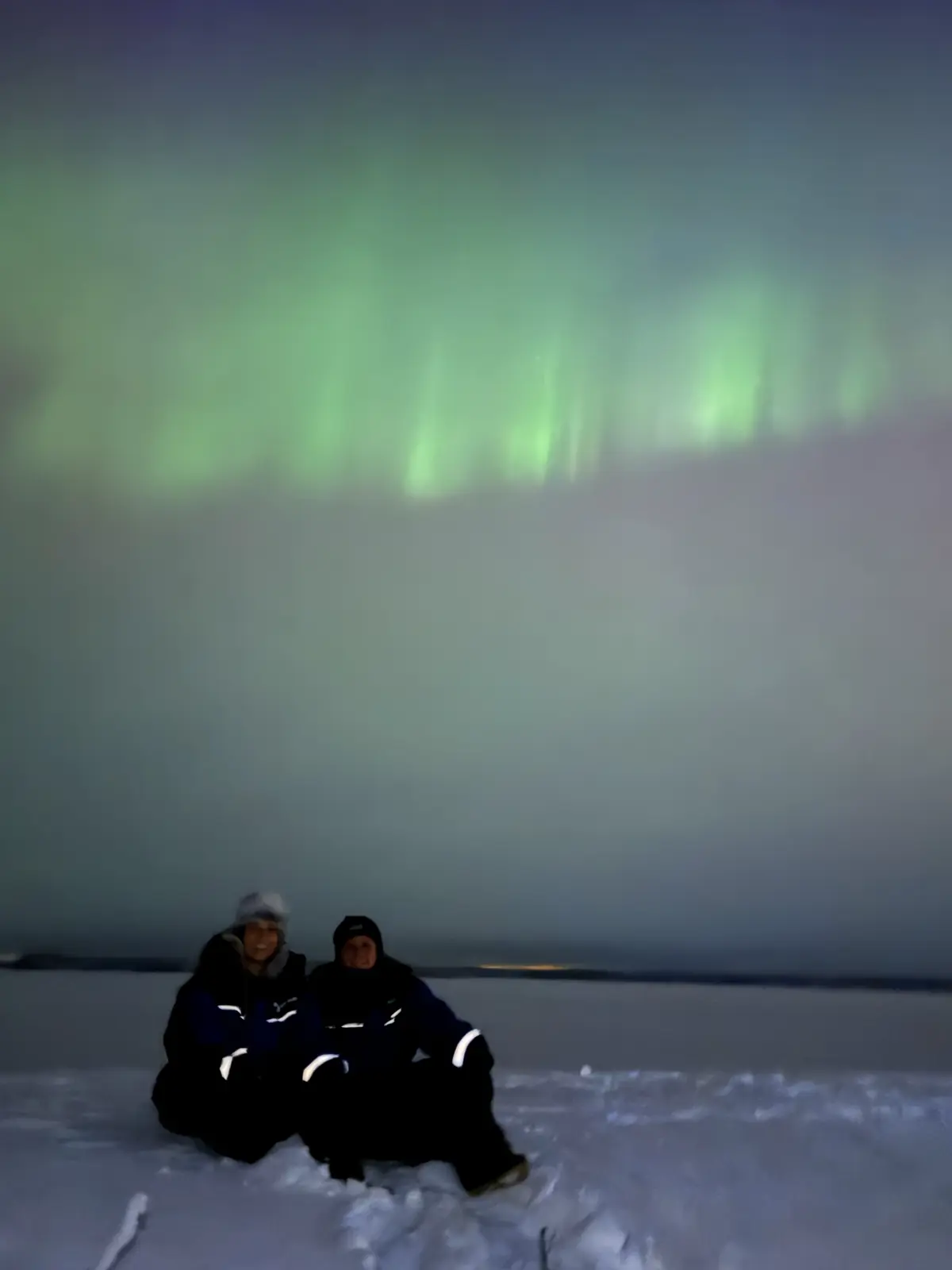 Viajeros sentados en la nieve mirando la aurora